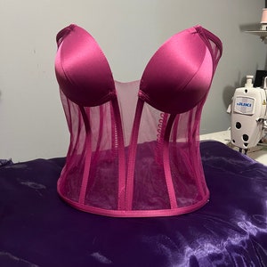 May include: A pink satin and mesh corset with boning and a plunging neckline.