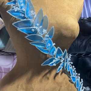 Könnte beinhalten: Ein blauer und silberner, blattartiger Schmuck mit klaren Perlen, perfekt, um einem Kleidungsstück oder Accessoire einen Hauch von Glanz zu verleihen.