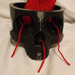 May include: A black skull-shaped yarn bowl with red yarn coming out of the eye sockets and nose hole.