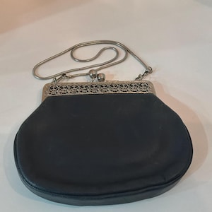 Pu&ograve; includere: Una borsa nera vintage con una tracolla a catena in metallo argentato. La borsa ha una forma arrotondata con una chiusura decorativa in metallo. La chiusura presenta un design traforato e intricato. La borsa &egrave; realizzata in un materiale scuro e liscio.