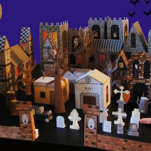 May include: A papercraft Halloween village with houses, trees, and a cemetery. The village is lit by a full moon and has a spooky atmosphere.