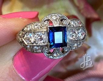 May include: A vintage-style engagement ring with a large, square-cut sapphire surrounded by smaller diamonds. The ring is set in a delicate, filigree design.