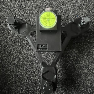 May include: A black, Y-shaped tool with a spirit level and adjustment knobs. The level has a green liquid and markings. The tool appears to be made of plastic, designed for precision work.