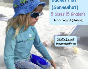 May include: A blue crocheted bucket hat with green toy trucks embroidered on it. The hat is for children and comes in 5 sizes. The hat is shown on a child sitting on a beach.