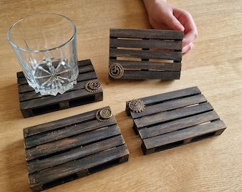 May include: Four wooden coasters with a distressed brown finish and metal gears. The coasters are shaped like miniature pallets.