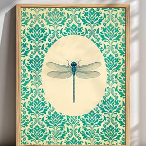 Peut inclure: Une impression d'art encadrée représentant une libellule bleue centrale placée dans un ovale crème. L'arrière-plan entourant l'ovale se compose d'un motif damassé sarcelle répétitif. L'ensemble est encadré dans un cadre en bois clair.