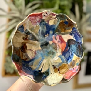 以下が含まれることがあります： 青、茶色、赤、白の色合いで、抽象的なデザインが施された、波打つ縁のあるセラミックボウルです。