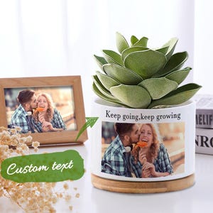 May include: White ceramic planter with a wooden base, featuring a green succulent plant and a photo of a couple kissing. The planter has the text "Keep going, keep growing" printed on the side.