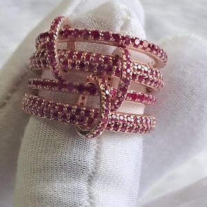 May include: A rose gold ring with multiple bands set with red cubic zirconia stones.