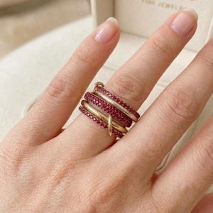 Pu&ograve; includere: Un anello a pi&ugrave; strati caratterizzato da fasce alternate in oro lucido e fasce incastonate con piccole pietre rosse vivaci. Il design &egrave; composto da diversi anelli interconnessi che si avvolgono attorno al dito, creando un aspetto sovrapposto con un mix di superfici metalliche lisce e segmenti testurizzati ricoperti di pietre preziose.
