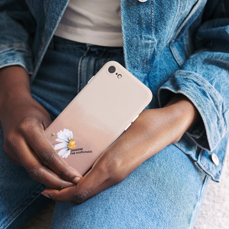 May include: A light pink phone case with a white daisy and the text "Consider the wildflowers".