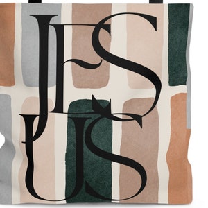 May include: A tote bag with a white background and abstract shapes in shades of brown, green, and gray. The word "JESUS" is written in black script over the shapes.