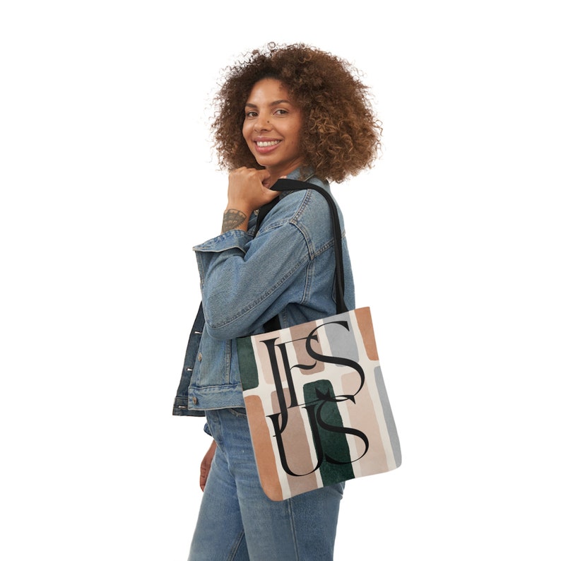 May include: A woman is holding a tote bag with a colorful abstract design and the word "JESUS" printed in black letters.