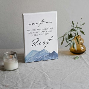 Pode incluir: Uma impressão em tela branca com uma cena de montanha aquarela azul. O texto "come to me" está escrito em itálico preto. O texto "ALL YOU WHO LABOR AND ARE HEAVY LADEN, AND I WILL GIVE YOU Rest" está escrito em preto. O texto "Matthew 11:28" está escrito em preto na parte inferior da impressão.