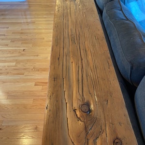 Pu&ograve; includere: Primo piano di uno scaffale in legno rustico con nodi e motivi a venature. Lo scaffale &egrave; attaccato a un divano grigio.