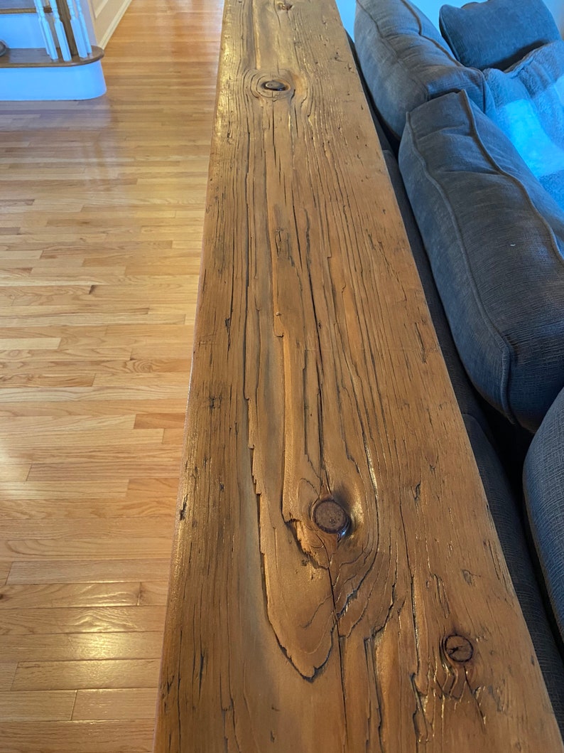 Pu&ograve; includere: Primo piano di uno scaffale in legno rustico con nodi e motivi a venature. Lo scaffale &egrave; attaccato a un divano grigio.