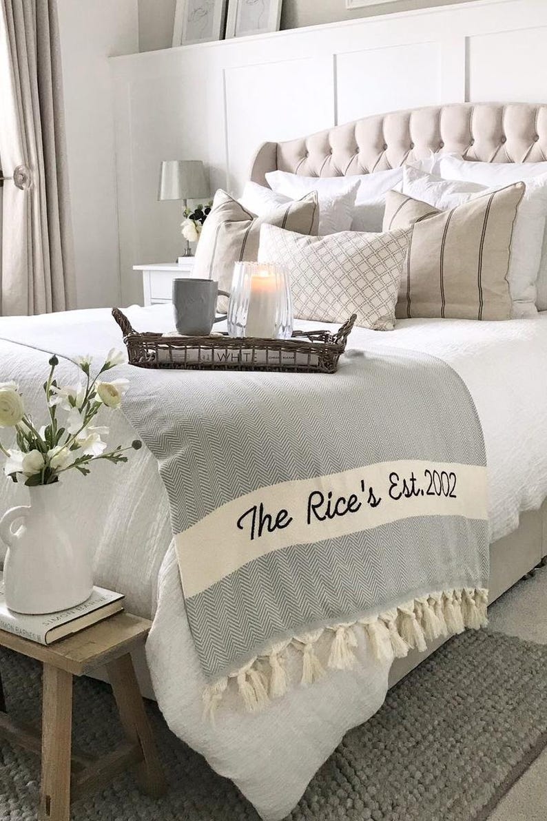 Puede incluir: Un dormitorio con una cama con s&aacute;banas y almohadas blancas. Una manta de espiga gris y blanca con el texto "The Rice's Est. 2002" est&aacute; sobre la cama. Una bandeja con una taza y una vela est&aacute; sobre la cama.