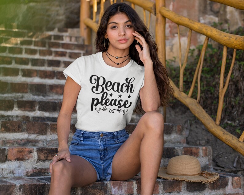 May include: A white t-shirt with the text "Beach Please" in black lettering with three stars above the word "Please". The shirt is being worn by a person sitting on a brick staircase.