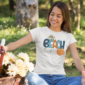 May include: A white t-shirt with a blue, orange, and green graphic that says "Beach Please" with palm trees.