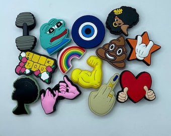 May include: A collection of colorful shoe charms in various shapes. Includes a dumbbell, a sad frog, a blue eye, a woman's silhouette, a poop emoji, a star with a hand gesture, a block with the text "F.Y.O.U.K.", a rainbow, a flexing arm, a hand with a middle finger, and a red heart.