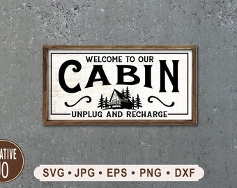 May include: A white wooden sign with black text that reads "Welcome to our Cabin - Unplug and Recharge". The sign features a black silhouette of a cabin with trees in front of it.