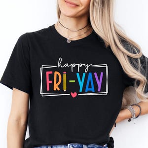 May include: Black t-shirt with the words "happy FRI-YAY" in a colorful, outlined font. The text is inside a white rectangular frame with a small heart. The shirt is worn with blue jeans.