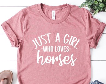Puede incluir: Una camiseta rosa con el texto "Just a girl -who loves- horses" en letras blancas.