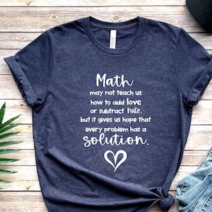 May include: A navy blue t-shirt with a white graphic that reads "Math may not teach us how to add love or subtract hate, but it gives us hope that every problem has a solution." A white heart is below the text.