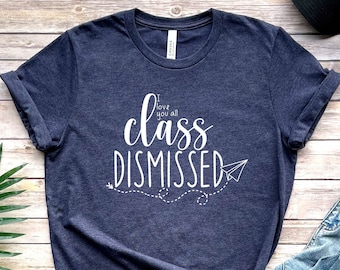 Puede incluir: Una camiseta azul marino con texto blanco que dice "I love you all class dismissed" con un gráfico de avión de papel.