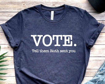 Op de afbeelding: Een donkerblauw T-shirt met witte tekst die "VOTE. Tell them Ruth sent you." zegt.