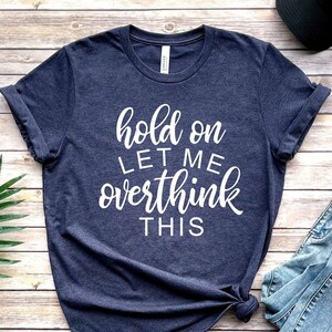 Pode incluir: Uma camiseta azul marinho com o texto "hold on let me overthink this" em letras brancas.
