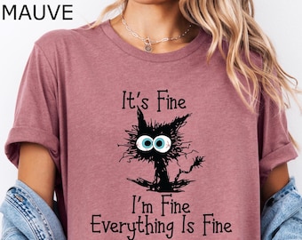 Puede incluir: Camiseta de color malva jaspeado con una ilustración de un gato negro y el texto "It's Fine I'm Fine Everything Is Fine."