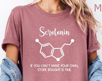 Puede incluir: Una camiseta de color malva con un gráfico blanco de la estructura química de la serotonina y el texto "Serotonina. Si no puedes hacerla tú mismo, la que se compra en la tienda está bien."