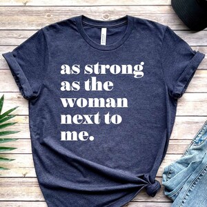 May include: A navy blue t-shirt with the text "as strong as the woman next to me." printed in white.