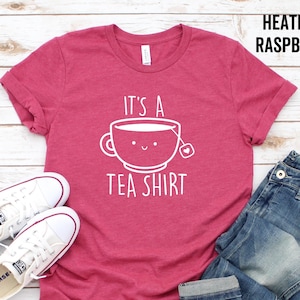 May include: A heather raspberry t-shirt with the text "It's a Tea Shirt" and a cartoon teacup with a smiling face.