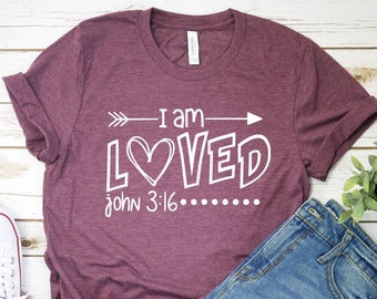 May include: A maroon t-shirt with a white graphic that says "I am LOVED" with an arrow pointing to the right and a heart in the "O". The text "John 3:16" is below the graphic.