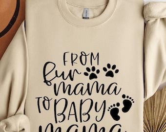 May include: Sand-colored sweatshirt with the text "FROM fur mama TO BABY mama" in black script. The design includes paw prints and baby footprints. The sweatshirt has a crew neck and long sleeves.