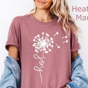 K&ouml;nnte beinhalten: Ein T-Shirt in der Farbe Heather Mauve mit einem wei&szlig;en L&ouml;wenzahnmuster und dem Wort "Hope" in Kursivschrift.