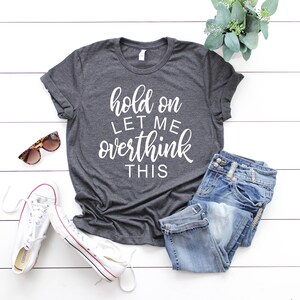 Pode incluir: Uma camiseta cinza escura com o texto "hold on let me overthink this" em letras brancas.
