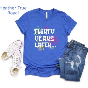 May include: A royal blue t-shirt with the text "Thirty Years Later..." in white with colorful flowers around the text.