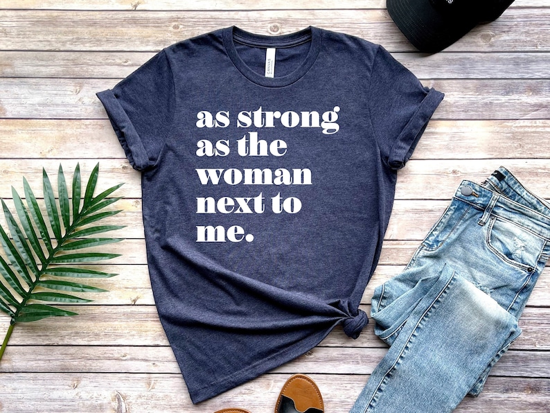 May include: A navy blue t-shirt with the text "as strong as the woman next to me." printed in white.