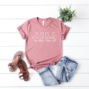 May include: A mauve t-shirt with a white graphic of three cats and the text "un deux trois cat".
