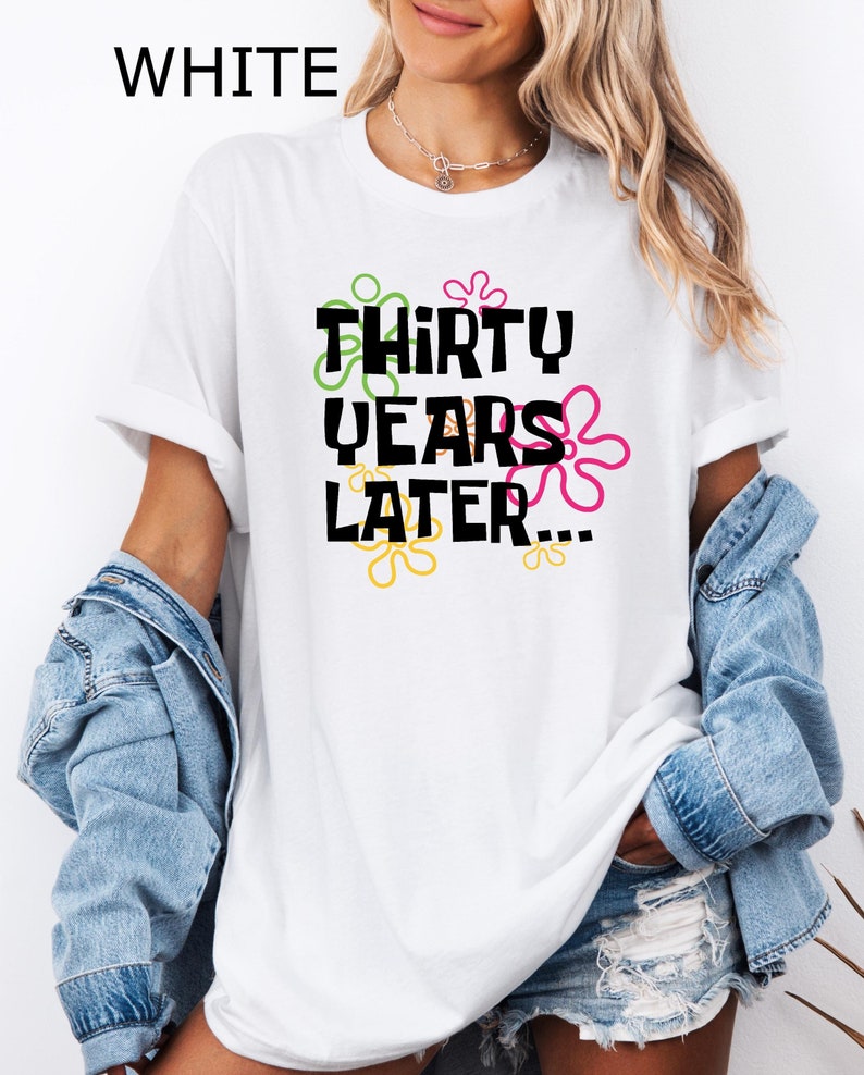 May include: White t-shirt with the text "Thirty Years Later..." in black lettering with colorful flower-like shapes around the text.