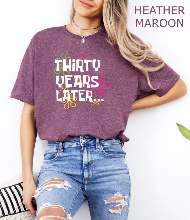 May include: A heather maroon t-shirt with the text "Thirty Years Later..." in white with colorful swirls around the text.