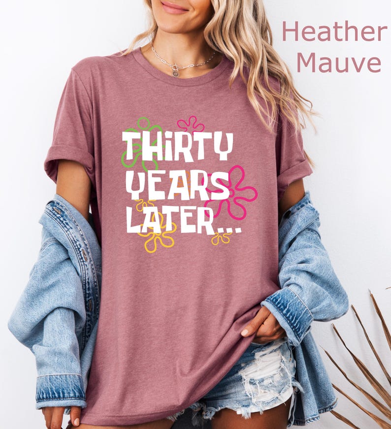 May include: Heather mauve t-shirt with a white graphic that says "Thirty Years Later..." with colorful flowers around the text.