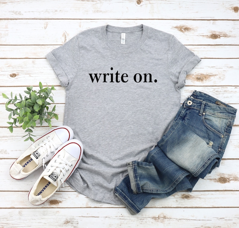 May include: A gray t-shirt with the text "write on." printed in black. The shirt is paired with blue jeans and white sneakers.