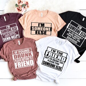Puede incluir: Cinco camisetas con frases humor&iacute;sticas sobre estar borracho. Las camisetas son de varios colores, incluyendo negro, blanco, rosa y marr&oacute;n. El texto en las camisetas dice: "Soy alguien m&aacute;s, pero probablemente estoy m&aacute;s borracho que ellos, &iexcl;env&iacute;a ayuda!" "Soy alguien m&aacute;s" "Soy alguien m&aacute;s, pero probablemente estoy m&aacute;s borracho que ellos, s00000" "Si se encuentra borracho, por favor regrese al amigo" "Soy el amigo, pero tambi&eacute;n estoy borracho, por favor encuentre a alguien m&aacute;s"