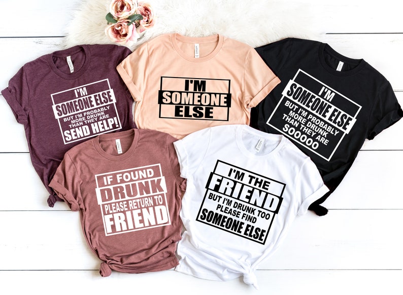 Puede incluir: Cinco camisetas con frases humor&iacute;sticas sobre estar borracho. Las camisetas son de varios colores, incluyendo negro, blanco, rosa y marr&oacute;n. El texto en las camisetas dice: "Soy alguien m&aacute;s, pero probablemente estoy m&aacute;s borracho que ellos, &iexcl;env&iacute;a ayuda!" "Soy alguien m&aacute;s" "Soy alguien m&aacute;s, pero probablemente estoy m&aacute;s borracho que ellos, s00000" "Si se encuentra borracho, por favor regrese al amigo" "Soy el amigo, pero tambi&eacute;n estoy borracho, por favor encuentre a alguien m&aacute;s"