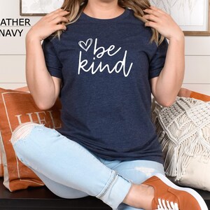 May include: A heather navy blue t-shirt with the text "be kind" in white lettering and a small heart graphic above the text.