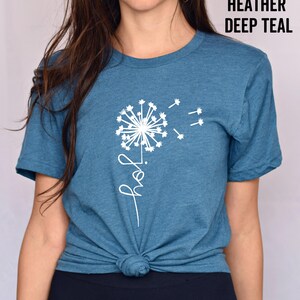 K&ouml;nnte beinhalten: Ein T-Shirt in der Farbe Heide-Tiefblau mit einem wei&szlig;en L&ouml;wenzahnmuster und dem Wort "Freude" in kursiv.